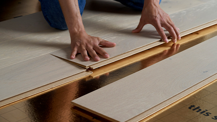 man installing a grey hardwood floor on an underlay